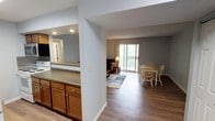 This single-floor residence offers a thoughtfully designed open-concept layout that seamlessly connects the kitchen, dining, and living areas into one cohesive living space. The kitchen features warm wood cabinetry with brushed hardware and a granite-look countertop, complemented by recessed lighting that brightens the workspace. A large pass-through opening visually links the kitchen to the main living area, enhancing the sense of openness throughout.

The dining area is situated adjacent to the kitchen and accommodates a classic wooden table and chair set, making it ideal for everyday meals or casual entertaining. Flowing naturally from the dining space, the living room is anchored by a sliding glass door that fills the area with natural light and provides direct access to an outdoor balcony or patio, offering views of surrounding greenery.

Durable wood-look flooring runs throughout the main living areas, adding warmth and continuity to the space. The neutral gray wall tones create a calm, versatile backdrop that complements the natural wood finishes. A textured ceiling and clean white trim complete the interior details. The overall ambiance is comfortable, practical, and bright, with a layout well-suited for everyday living.