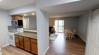 This single-floor residence offers a thoughtfully designed open-concept layout that seamlessly connects the kitchen, dining, and living areas into one cohesive living space. The kitchen features warm wood cabinetry with brushed hardware and a granite-look countertop, complemented by recessed lighting that brightens the workspace. A large pass-through opening visually links the kitchen to the main living area, enhancing the sense of openness throughout.

The dining area is situated adjacent to the kitchen and accommodates a classic wooden table and chair set, making it ideal for everyday meals or casual entertaining. Flowing naturally from the dining space, the living room is anchored by a sliding glass door that fills the area with natural light and provides direct access to an outdoor balcony or patio, offering views of surrounding greenery.

Durable wood-look flooring runs throughout the main living areas, adding warmth and continuity to the space. The neutral gray wall tones create a calm, versatile backdrop that complements the natural wood finishes. A textured ceiling and clean white trim complete the interior details. The overall ambiance is comfortable, practical, and bright, with a layout well-suited for everyday living.