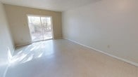 This single-floor space offers a clean, functional layout with a straightforward design aesthetic. The main living area is open and generously proportioned, featuring light-toned tile flooring that spans the room and contributes to an overall sense of spaciousness. Walls are finished in a soft, neutral beige and white palette, providing a versatile backdrop well-suited for a variety of uses.

A standout feature of the living area is the large sliding glass door, which serves as both a primary source of natural light and a direct connection to the outdoors. The view beyond reveals a natural, wooded setting, offering privacy and a serene outdoor backdrop. Sunlight filters through the glass door, casting natural light across the tile floor and brightening the interior throughout the day.

The ceiling features a subtle textured finish, and clean white baseboards line the perimeter of the room, adding a crisp, finished look to the space. The overall ambiance is calm and understated, with minimal ornamentation that allows the architectural simplicity to speak for itself. The space presents a practical, move-in-ready environment with ample room to customize and configure according to individual needs.