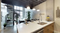 This two-story urban loft blends industrial character with modern comfort in a striking and cohesive design. The main living area commands attention with soaring ceilings, exposed steel beam details, and floor-to-ceiling windows that flood the space with natural light and offer sweeping views of the surrounding cityscape. A sculptural spiral staircase serves as both a functional and architectural centerpiece, linking the two floors with style.

The open-concept kitchen features warm wood-grain cabinetry paired with crisp white quartz countertops, a large stainless steel double sink, a professional-grade gas range, built-in microwave, and a full-size stainless steel refrigerator. Polished concrete floors and pendant lighting complete the contemporary aesthetic.

The bedrooms carry the industrial theme through raw concrete walls and exposed conduit piping, softened by large windows with urban views and thoughtful furnishing. A walk-in closet provides generous built-in storage. The bathrooms are well-appointed, featuring a glass-enclosed shower, a soaking tub with large-format tile surround, wood-look flooring, and clean, neutral finishes. An in-unit laundry closet with a full-size washer and dryer adds everyday convenience. Throughout, the space strikes a compelling balance between raw industrial design and refined livability.