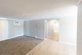 Located at 59 State St in Tully, NY, this single-floor unit offers five bedrooms and one bathroom within a well-organized layout. The living area features a combination of soft carpeting and light wood-style flooring, with neutral gray walls and clean white trim throughout. Wall-mounted air conditioning and baseboard heating units provide year-round climate control. The galley-style kitchen is a standout feature, equipped with two-tone cabinetry — white upper cabinets and gray lower cabinets — paired with granite countertops, stainless steel appliances including a range, microwave, and refrigerator, and a double-basin sink. The bathroom echoes the kitchen's refined aesthetic with a granite-topped vanity, a wall-mounted medicine cabinet with integrated lighting, and light wood-style flooring. Each of the five bedrooms is carpeted and finished with neutral tones, offering a clean and functional space. Several bedrooms include windows that bring in natural light and views of the surrounding area. A connecting hallway ties the rooms together, creating a straightforward and accessible floor plan throughout this well-maintained Tully, NY residence.
