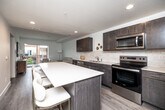 Located at 317 E Sixth St in the heart of Des Moines, Iowa, this thoughtfully designed 2-bedroom, 1-bathroom residence offers a contemporary open-concept layout on a single floor. The kitchen is a standout feature, equipped with dark espresso cabinetry, white quartz countertops, a classic subway tile backsplash, and a full suite of stainless steel appliances including a refrigerator, range, microwave, and dishwasher. A central kitchen island with bar seating provides additional workspace and a natural gathering point. The kitchen flows seamlessly into the living room, which is bathed in natural light and opens onto a private balcony through sliding glass doors, offering views of the surrounding neighborhood. Light wood-tone flooring runs throughout, enhancing the bright and airy ambiance. The primary bedroom is a comfortable retreat featuring a ceiling fan, large windows with urban views, and ample space. The second bedroom is equally well-lit with a large window. The full bathroom is finished with dark wood floating vanity cabinetry, a white countertop, a large mirror, and wood-look tile flooring, maintaining the clean, modern aesthetic found throughout the residence.