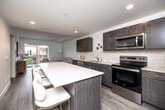 Located at 317 E Sixth St in the heart of Des Moines, Iowa, this thoughtfully designed 2-bedroom, 1-bathroom residence offers a contemporary open-concept layout on a single floor. The kitchen is a standout feature, equipped with dark espresso cabinetry, white quartz countertops, a classic subway tile backsplash, and a full suite of stainless steel appliances including a refrigerator, range, microwave, and dishwasher. A central kitchen island with bar seating provides additional workspace and a natural gathering point. The kitchen flows seamlessly into the living room, which is bathed in natural light and opens onto a private balcony through sliding glass doors, offering views of the surrounding neighborhood. Light wood-tone flooring runs throughout, enhancing the bright and airy ambiance. The primary bedroom is a comfortable retreat featuring a ceiling fan, large windows with urban views, and ample space. The second bedroom is equally well-lit with a large window. The full bathroom is finished with dark wood floating vanity cabinetry, a white countertop, a large mirror, and wood-look tile flooring, maintaining the clean, modern aesthetic found throughout the residence.