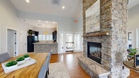 Located at 280 Cumberland Trace Rd in Bowling Green, Kentucky, this single-floor space offers a thoughtfully designed open-concept layout that maximizes both functionality and visual appeal. The centerpiece of the space is a striking floor-to-ceiling stacked-stone fireplace with a rustic wood mantel, serving as a dramatic architectural focal point that anchors the living area. Soaring vaulted ceilings amplify the sense of openness throughout, while warm hardwood floors run consistently across the entire space, adding richness and cohesion to the interior.

The living area is generously sized, featuring multiple seating arrangements, large windows that invite abundant natural light, and views of the surrounding greenery. A welcoming entrance greets visitors with glass-paneled French doors, creating a bright and airy transition into the main living space. A dedicated dining area accommodates a solid wood farmhouse-style table, positioned adjacent to windows that further enhance the natural light.

A kitchen with dark cabinetry, pendant lighting, and a stone-accented island is visible from the main living area, reinforcing the open flow of the space. A glass-windowed interior office nook provides a semi-private workspace without sacrificing connectivity to the broader environment. Neutral gray walls and recessed lighting throughout complete the clean, modern aesthetic of this inviting space.