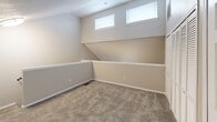 This two-story residence in Wichita, Kansas offers a well-organized layout spread across two floors. The main level features a kitchen equipped with gray cabinetry, granite-look countertops, a stainless steel refrigerator, electric range, and a double stainless steel sink. Wood-style plank flooring runs throughout the main level, adding warmth and durability. A staircase connects the main level to the upper floor, where both bedrooms are located. The primary bedroom is a comfortable size, featuring soft carpeting and a ceiling fan with integrated lighting. The second bedroom also includes carpet flooring, a ceiling fan, a window with natural light, and a closet with built-in shelving. A uniquely shaped secondary room on the upper level showcases angular, sloped walls and high clerestory windows that draw in additional natural light, lending an architectural character to the space. The full bathroom is finished with wood-style tile flooring, a granite-look vanity with gray cabinetry, a full tub-shower combination, and brushed nickel fixtures and hardware. Throughout the unit, neutral wall tones and clean white trim create a cohesive, move-in-ready aesthetic that is both practical and inviting.