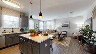 This single-floor residence at 100 Oakview Dr in Trumbull, Connecticut, offers a thoughtfully designed open-concept layout that seamlessly connects the kitchen, dining, and living areas. The kitchen is a standout feature, showcasing gray shaker-style cabinetry, white quartz countertops, a classic subway tile backsplash, and a full suite of stainless steel appliances including a gas range, built-in microwave, dishwasher, and French door refrigerator. A central island with pendant lighting provides additional prep space and casual seating. The living area is bright and spacious, with wood-look flooring flowing throughout and large windows that invite abundant natural light. A dedicated dining nook, surrounded by multiple windows with sheer curtains, creates an airy and pleasant space for meals. The bedroom features wood-look flooring, neutral walls, and access to a generous walk-in closet. Two bathrooms serve the residence: one with a glass-enclosed walk-in shower and tiled surround, and another with a tub-shower combination — both finished with gray vanities, white countertops, and tile flooring. The overall aesthetic is modern and cohesive, with warm metallic accents and a neutral color palette throughout.