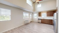 This well-designed 2-bedroom, 2-bathroom unit makes efficient use of its single-floor layout, offering a bright and modern living environment. The open-concept living and kitchen area is immediately distinguished by dramatically vaulted ceilings that amplify the sense of space, complemented by clerestory windows positioned high on the walls to draw in abundant natural light. A ceiling fan serves both the aesthetic and functional needs of the room, while a wall-mounted HVAC unit provides dedicated climate control. Multiple windows at standard height overlook the surrounding neighborhood, further enhancing the airy atmosphere.

The kitchen is outfitted with a full suite of stainless steel appliances—including a refrigerator, range, microwave, and dishwasher—paired with warm wood-toned cabinetry and clean white countertops arranged in an efficient L-shaped configuration.

Both bedrooms feature light wood-look flooring consistent with the rest of the unit, neutral walls, and windows that provide natural light and outdoor views. The primary bedroom benefits from an en-suite bathroom with a walk-in closet featuring built-in shelving and rod storage. A second bathroom includes a single vanity with wood cabinetry, a large mirror, and a shower-tub combination.