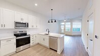 This well-appointed 2-bedroom, 1-bathroom residence offers a thoughtfully designed single-floor layout with a clean, contemporary aesthetic. The open-concept kitchen and living area serves as the heart of the home, featuring crisp white shaker cabinetry with matte black hardware, a white quartz peninsula with an undermount sink, and a full suite of stainless steel appliances including a refrigerator, electric range, microwave, and dishwasher. A modern three-light pendant fixture anchors the kitchen, while recessed lighting and a ceiling fan in the living area enhance both function and comfort. Light wood-tone flooring flows seamlessly throughout the entire unit, contributing to a bright and cohesive feel. The living room opens directly to a private balcony through a glass-panel door, allowing for natural light and outdoor access. Both bedrooms are well-sized with neutral walls and large windows dressed with roller shades. The primary bedroom benefits from a spacious walk-in closet complete with built-in shelving and hanging rods. The full bathroom features a tub-shower combination with white tile surround, matte black fixtures, and a vanity with white cabinetry. A dedicated hallway and additional closet space round out this clean, move-in-ready residence.
