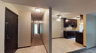 This single-story space is defined by a long, carpeted hallway that stretches toward the back of the unit, lined with closet doors that offer ample built-in storage. Flush-mount ceiling lights illuminate the corridor, creating a clean and functional passageway connecting the various rooms. The hallway transitions into the main living and kitchen area, where light tile flooring contrasts with the warm carpet of the hall. The kitchen features dark espresso-toned cabinetry both above and below the counter, paired with a granite-look countertop and a sink positioned along the back wall. A ceiling fan with an integrated light fixture is centrally mounted overhead, providing both airflow and ambient lighting to the space. The textured ceilings are consistent throughout, adding subtle depth to the interior. The overall layout is practical and straightforward, with clearly defined zones for living and utility. The dark cabinetry against the neutral walls and light flooring creates a balanced contrast that anchors the kitchen area visually. The space is well-suited for everyday functionality with a modest, no-frills design aesthetic.