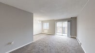 This one-bedroom, one-bathroom unit at 2701 Madison St in Chester, PA offers a practical and well-organized layout across a single floor. The living room is generously sized, featuring soft carpeted flooring, neutral gray walls, and a textured ceiling. Large sliding glass doors open to a private balcony, allowing natural light to fill the space and providing outdoor views. A pendant chandelier accents the adjacent dining area, which features light hardwood-style flooring and a bright window with blinds, creating a welcoming transition between spaces. The bedroom is a comfortable size, fitted with plush carpet, gray walls, a window for natural light, and a built-in closet with shelving for ample storage. A hallway connects the main living areas to the full bathroom, which is finished in clean white with a tub-shower combination, vanity sink, and large mirror. Baseboard heating is present throughout the unit. The entry area provides a practical foyer space with carpeted flooring and direct access to the main living zone. Overall, the unit presents a clean, neutral aesthetic that is move-in ready, with functional room arrangements and consistent finishes throughout.