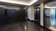 Located at 44 Maryland Ave in Rockville, Maryland, this contemporary fitness studio is designed with a refined, upscale aesthetic that balances functionality with sophisticated style. The space is defined by rich, dark hardwood flooring that reflects the ambient lighting overhead, creating a polished and energizing atmosphere throughout.

The studio is framed by a coffered ceiling with elegant cove lighting and recessed spotlights that illuminate the space evenly. Full-length glass-panel sliding doors serve as a striking architectural feature, allowing views into the main workout area while maintaining an open, airy feel. TRX suspension training straps are mounted and ready for use, underscoring the space's focus on versatile fitness training.

Dark slatted wall panels and large mirrors are positioned strategically to enhance the sense of depth and allow users to monitor their form during workouts. A dedicated equipment alcove features built-in shelving stocked with yoga mats, stability balls, and other fitness accessories, alongside a sleek storage cabinet topped with a work surface and accented by framed athletic artwork above.

An integrated display screen mounted on the dark feature wall adds a modern, tech-forward element to the studio. The overall design combines premium materials, thoughtful lighting, and purposeful layout to deliver a high-end fitness environment suited for a variety of training modalities.