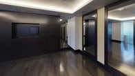 Located at 44 Maryland Ave in Rockville, Maryland, this contemporary fitness studio is designed with a refined, upscale aesthetic that balances functionality with sophisticated style. The space is defined by rich, dark hardwood flooring that reflects the ambient lighting overhead, creating a polished and energizing atmosphere throughout.

The studio is framed by a coffered ceiling with elegant cove lighting and recessed spotlights that illuminate the space evenly. Full-length glass-panel sliding doors serve as a striking architectural feature, allowing views into the main workout area while maintaining an open, airy feel. TRX suspension training straps are mounted and ready for use, underscoring the space's focus on versatile fitness training.

Dark slatted wall panels and large mirrors are positioned strategically to enhance the sense of depth and allow users to monitor their form during workouts. A dedicated equipment alcove features built-in shelving stocked with yoga mats, stability balls, and other fitness accessories, alongside a sleek storage cabinet topped with a work surface and accented by framed athletic artwork above.

An integrated display screen mounted on the dark feature wall adds a modern, tech-forward element to the studio. The overall design combines premium materials, thoughtful lighting, and purposeful layout to deliver a high-end fitness environment suited for a variety of training modalities.