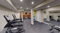 Located at 5284 Marlboro Pike in Capitol Heights, Maryland, this dedicated fitness facility offers a thoughtfully designed workout space built to accommodate a comprehensive exercise routine. The gym features durable speckled rubber flooring throughout, providing a safe and functional surface ideal for all types of training activities.

The space is divided into distinct workout zones, each serving a specific fitness purpose. The cardio area is outfitted with multiple treadmills, an elliptical, and a recumbent exercise bike from True Fitness, offering a full range of cardiovascular training options. A multi-station cable and weight machine anchors the strength training section, providing versatility for a wide variety of resistance exercises.

Structural columns are integrated cleanly into the layout and are finished with crisp white bases, contributing to the space's polished, professional aesthetic. The walls are painted in a neutral warm beige, complemented by an accent wall in a rich terracotta tone that adds visual interest. Large mirrors are strategically positioned along the walls to support proper exercise form and enhance the sense of openness.

Recessed lighting illuminates the space evenly throughout, creating a bright and energizing environment. Stability balls and additional fitness accessories are neatly stored, and a hand sanitizer dispenser reflects attention to hygiene. Multiple doors provide access to adjoining areas, adding convenience and functionality to this well-appointed fitness space.