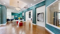 Located at 1699 Chatham Pkwy in Savannah, Georgia, this single-floor community clubhouse makes a striking first impression with its bold, teal-patterned accent walls, warm hardwood flooring, and soaring double-height ceilings. The main entry area is anchored by a glamorous crystal chandelier and open archways framed in rich teal tilework, setting a vibrant yet sophisticated tone throughout the space.

The expansive living area serves as the social centerpiece, featuring a dramatic floor-to-ceiling stacked stone fireplace, plush seating arrangements, and large windows that invite natural light. A billiards table and a game table with upholstered seating provide ample recreational options. Adjacent to this is a dedicated lounge featuring eye-catching black-and-white graphic wallpaper, bold red patterned carpet, and eclectic seating — creating a distinctive, artistic atmosphere.

The clubhouse also includes a professional-style workspace with multiple desk stations and blue upholstered chairs, ideal for residents seeking a productive environment. A well-equipped fitness center, visible through a large interior window, offers a variety of exercise equipment including a climbing wall and strength machines. French doors throughout connect the interior to the outdoors, enhancing the sense of openness and flow across this thoughtfully designed, amenity-rich community space.