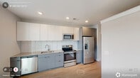 Located at 318 W Corporation St in the heart of Durham, NC, this thoughtfully designed one-bedroom, one-bathroom residence offers a clean, modern aesthetic throughout its efficiently arranged single-floor layout. Light wood-tone flooring runs continuously through the space, complementing the crisp white walls and recessed lighting that keep the interior bright and welcoming.

The open kitchen is a standout feature, equipped with a full suite of stainless steel appliances — including a refrigerator with ice maker, electric range, microwave, and dishwasher — paired with two-tone cabinetry in white and slate gray, granite countertops, and a white subway tile backsplash. A dedicated laundry area adds everyday convenience.

The living room is bathed in natural light from a set of large floor-to-ceiling windows that frame views of the surrounding Durham cityscape. The bedroom offers a ceiling fan, a walk-in closet with built-in shelving, and a calm, neutral palette. The bathroom features a walk-in glass-enclosed shower with white stacked tile, matte black hardware accents, a granite-topped vanity, and wood-look tile flooring. A central hallway with barn-style doors connects the spaces, lending a contemporary touch to the overall design.