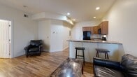 Located at 1055 Philadelphia St in Indiana, Pennsylvania, this single-floor unit offers a well-organized and functional layout designed for comfortable everyday living. The open-concept living and kitchen area serves as the heart of the space, where warm hardwood flooring flows seamlessly throughout. Recessed lighting illuminates the living room, which features an arched architectural detail that adds character to the open floor plan.

The kitchen is fully equipped with black appliances, including an electric range, over-the-range microwave, and refrigerator. Ample warm-toned wood cabinetry provides generous storage, while granite-style countertops extend to a breakfast bar with bar seating — ideal for casual dining or entertaining.

The two bedrooms are comfortably sized and share the same consistent hardwood flooring. Each room benefits from large windows with blinds that allow natural light to fill the space while offering views of the surrounding neighborhood. The bedrooms provide a quiet and functional retreat.

The full bathroom is clean and efficiently designed, featuring a combination tub and shower, a wood-cabinet vanity with a white countertop, and a wall-mounted towel rack. Neutral wall tones and consistent flooring throughout the unit create a cohesive and inviting ambiance from room to room.