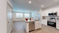 This thoughtfully designed single-floor residence offers a clean, modern aesthetic with light-toned luxury vinyl plank flooring running consistently throughout every room. The open-concept layout connects the kitchen and living area seamlessly, creating a bright and functional shared space anchored by a central kitchen island with granite countertops, an undermount sink, and a stainless steel dishwasher. White shaker cabinetry lines the kitchen walls, complemented by a stainless steel French door refrigerator and recessed lighting overhead. The living area benefits from two large windows that invite natural light and is equipped with a ceiling fan for added comfort. The bedroom is a well-sized, tranquil retreat featuring its own ceiling fan, a large window with blinds, and direct access to a dedicated walk-in closet outfitted with wire shelving and hanging rods on multiple walls. The bathroom showcases a granite-topped vanity with white cabinetry, a large mirror, and a full tub/shower combination with striking marble-style wall surrounds. Neutral wall tones and consistent flooring throughout lend the space a cohesive, contemporary feel that is both functional and inviting.