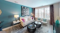 Located at 15250 Siesta Key Way in Rockville, Maryland, this single-floor residence offers a thoughtfully designed interior defined by bold color choices, modern finishes, and a cohesive decorative style. The living area serves as the centerpiece of the home, featuring a striking teal accent wall adorned with contemporary artwork. Large windows invite generous natural light, complementing the space's vibrant energy. Stylish furnishings, including a classic cream sofa with fuchsia accent pillows, sculptural glass coffee tables, and an eye-catching multi-globe floor lamp, give the room a sophisticated yet inviting character. The kitchen is well-appointed with crisp white cabinetry, granite countertops, stainless steel appliances, and light wood-look flooring that extends throughout the common areas, offering both durability and a warm aesthetic. The bedroom is a distinctly styled retreat, anchored by a deep purple accent wall and a sleek four-poster bed frame. Natural light filters through white-slatted blinds framed by patterned curtains, with views of an outdoor pool visible from the window. The bathroom continues the home's refined sensibility with granite countertops, clean white cabinetry, wood-look flooring, and vibrant teal patterned curtains surrounding the tub-shower combination. Every room reflects a carefully curated design that balances bold personality with functional comfort.