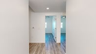 Located at 5055 N 19th Ave in Phoenix, AZ, this four-bedroom, one-bathroom single-story unit offers a clean, modern aesthetic throughout. Light-toned luxury vinyl plank flooring runs consistently across every room, contributing to a cohesive and low-maintenance living environment.

The combined kitchen and living area serves as the heart of the home. The kitchen is outfitted with white shaker-style cabinetry extending to the ceiling, gray countertops, and black appliances including a range, over-the-range microwave, and refrigerator. Recessed lighting illuminates the space efficiently.

Hallways connect the living areas to the four bedrooms, each of which features a ceiling fan, white walls, and windows that bring in natural light and offer views of the surrounding Phoenix neighborhood. The bedrooms are compact yet functional, with the primary bedroom providing a comfortable retreat.

The single shared bathroom includes a vanity with white cabinetry and a dark countertop, a toilet, and a glass-enclosed shower, all finished in the same neutral palette found throughout the home.

Two hallways provide practical circulation through the unit, with smart home thermostat controls visible along the walls. The overall design prioritizes clean lines, neutral tones, and modern finishes, making this a well-appointed and move-in-ready home in central Phoenix.