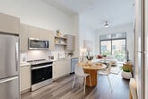 Located at 3440 SW 76 Terr in Davie, FL, this thoughtfully designed one-bedroom, one-bathroom residence offers a clean, modern aesthetic throughout its efficiently arranged single-floor layout. Soaring ceilings amplify the sense of openness in the combined kitchen and living area, where large floor-to-ceiling windows and a sliding glass door flood the space with natural light and provide direct access to a private balcony overlooking a lush, landscaped courtyard. The kitchen features flat-front cabinetry in a warm taupe finish, stainless steel appliances including a range, microwave, dishwasher, and refrigerator, complemented by a white tile backsplash and open shelving. Rich wood-look plank flooring runs seamlessly throughout the unit. A built-in desk nook provides a convenient workspace just off the main living area. The bedroom is a serene retreat with a window framing greenery views and a dedicated closet for storage. The bathroom impresses with a frameless glass walk-in shower clad in marble-style tile, a sleek vanity with white countertops, and matching wood-look flooring. Every detail reflects a commitment to contemporary comfort and refined, functional design.