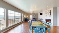Located at 2100 Rebsamen Park Rd in Little Rock, Arkansas, this single-floor space offers a thoughtfully designed open-plan layout that seamlessly integrates a dining area and living room into one cohesive environment. Rich hardwood flooring extends throughout, lending warmth and continuity to the space.

The dining area is anchored by a vibrant multicolored wood table paired with teal cross-back chairs, set atop a patterned area rug. A striking mid-century modern chandelier with exposed globe bulbs illuminates the area, adding a contemporary design element overhead. Large multi-pane windows line one wall, flooding the space with natural light and offering panoramic views of the surrounding landscape.

The living area features a white-painted fireplace as a central architectural focal point, flanked by tasteful artwork. Comfortable seating, including a bold blue sofa and gray upholstered chairs, is arranged around a clean-lined white coffee table on a neutral area rug. A wall-mounted flat-screen TV and a sleek console table complete the functional layout.

Neutral gray walls throughout provide a calm, versatile backdrop, while recessed lighting supplements the natural light. Two exterior doors with glass panels provide accessibility and additional light. The overall ambiance is modern, airy, and welcoming, making the space well-suited for both gatherings and everyday use.