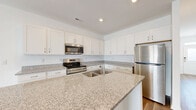 Located at 2108 Silty Soil Ct in Leland, NC, this two-story home offers four bedrooms and two bathrooms across two well-proportioned floors. The main level features an open-concept kitchen and living area bathed in natural light from sliding glass doors that lead to the outdoors. The kitchen is a standout space, appointed with crisp white shaker cabinetry, granite countertops, a central island with a double undermount sink, and a full suite of stainless steel appliances. Light-toned luxury vinyl plank flooring flows throughout, lending a clean and contemporary feel to the home. The living room is bright and airy, with a ceiling fan and sliding glass door access to the exterior. A staircase with a wood handrail connects to the upper level, where the bedrooms are situated. The generously sized primary bedroom offers comfortable proportions, while all bedrooms feature light-filled interiors and easy access to hallways. A dedicated closet provides well-organized storage with wire shelving. The bathrooms echo the home's consistent design language, featuring granite-topped vanities with white cabinetry and wood-look flooring. An attached garage with an automatic opener rounds out this well-appointed home.