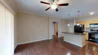 Located at 1202 Evans Rd in San Antonio, Texas, this single-floor residence offers a well-designed layout that balances comfort and functionality. The open-concept living area is finished with rich wood-look flooring and accented by elegant crown molding, creating a polished, cohesive aesthetic throughout. A ceiling fan provides year-round comfort, while vertical blinds on a sliding door allow for adjustable natural light. An arched passageway connects the living area to the rest of the unit, adding a distinctive architectural touch.

The kitchen is a functional centerpiece, featuring a large center island with a dark countertop, light wood cabinetry offering ample storage, and a full suite of black appliances including a refrigerator, range, built-in microwave, and dishwasher. Pendant lighting and track lighting illuminate the workspace effectively. The kitchen flows naturally into the living and dining areas, making it ideal for everyday use.

The bedrooms are carpeted for comfort and include ceiling fans and window blinds. The bathroom is appointed with a granite-topped vanity, a tiled tub-shower combination, and wood-look flooring. An attached garage with an automatic opener provides secure, private parking and additional storage space.