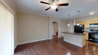 Located at 1202 Evans Rd in San Antonio, Texas, this single-floor residence offers a well-designed layout that balances comfort and functionality. The open-concept living area is finished with rich wood-look flooring and accented by elegant crown molding, creating a polished, cohesive aesthetic throughout. A ceiling fan provides year-round comfort, while vertical blinds on a sliding door allow for adjustable natural light. An arched passageway connects the living area to the rest of the unit, adding a distinctive architectural touch.

The kitchen is a functional centerpiece, featuring a large center island with a dark countertop, light wood cabinetry offering ample storage, and a full suite of black appliances including a refrigerator, range, built-in microwave, and dishwasher. Pendant lighting and track lighting illuminate the workspace effectively. The kitchen flows naturally into the living and dining areas, making it ideal for everyday use.

The bedrooms are carpeted for comfort and include ceiling fans and window blinds. The bathroom is appointed with a granite-topped vanity, a tiled tub-shower combination, and wood-look flooring. An attached garage with an automatic opener provides secure, private parking and additional storage space.