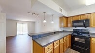 Located at 1000 Old Brook Road in Charlottesville, Virginia, this two-bedroom, two-bathroom single-floor residence offers a functional and comfortable layout. The open-concept kitchen is a central highlight, featuring warm honey-toned cabinetry, dark granite-style countertops, a full suite of black appliances including a range, microwave, and refrigerator, and a peninsula with pendant lighting that connects seamlessly to the living area. The living room benefits from natural light through vertical blinds and a sliding door, complemented by track lighting and easy-care hardwood-style flooring.

The two bedrooms offer distinct character: one is finished with plush carpeting and features a window with outdoor greenery views, a closet, and direct access to a full bathroom with a shower-tub combination. The second bedroom features hardwood-style flooring, crown molding, and access to natural light. Both bathrooms are well-appointed with wood-toned vanities and tile-style flooring. Three closets throughout the unit provide ample storage. A connecting hallway ties the layout together efficiently. The clean, neutral palette across all rooms creates a bright and adaptable living environment suitable for a variety of lifestyles.