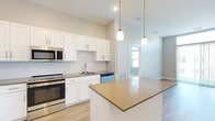 Located at 4 Tuscan Blvd in Salem, New Hampshire, this single-floor residence offers a thoughtfully designed layout with modern finishes throughout. The kitchen serves as a centerpiece of the home, featuring white shaker-style cabinetry, subway tile backsplash, quartz-style countertops, and a full suite of stainless steel appliances including a refrigerator, range, built-in microwave, and dishwasher. A center island with pendant lighting overhead provides additional prep space and casual seating, while light hardwood-style flooring ties the kitchen seamlessly into the adjacent living areas. The living and dining spaces are bright and open, benefiting from large sliding glass doors that invite natural light and offer outdoor access. Bedrooms are carpeted for comfort, with generous closet space including a walk-in closet with wire shelving. The bathrooms are finished with tile flooring, white vanity cabinetry, and dark countertops; one bathroom features a walk-in shower with a sliding glass door, while the other includes a shower-tub combination. An in-unit laundry area accommodates a side-by-side washer and dryer. The overall aesthetic is clean and contemporary, with neutral tones, crisp white trim, and consistent modern hardware throughout.