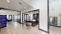 This residential clubhouse spans two floors and offers a thoughtfully designed layout with distinct functional areas. The entrance features light tile flooring, soaring ceilings, and a reception desk framed by bold black trim, creating a polished and professional first impression. French doors with dark frames allow natural light to flow throughout, enhancing the bright, clean aesthetic defined by crisp white walls throughout the space.

The living room is an inviting, open area furnished with a rich teal velvet sofa and complementary seating, set against large-format abstract artwork. Multiple French doors connect this room to the exterior, flooding it with natural light and providing views of the landscaped grounds. A ceiling fan and recessed lighting add to the comfort of the space.

The exercise room is outfitted with fitness equipment, large windows for natural light, and a striking hexagonal tile floor in blue and gray tones. Full-length mirrors expand the sense of space, while a ceiling fan keeps the area ventilated.

Outdoors, the community boasts a pool area flanked by palm trees, a covered patio with arched architectural detailing and ceiling fan, an outdoor grill station, and winding landscaped walkways — all contributing to a vibrant, resort-style atmosphere.