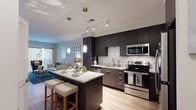 This thoughtfully designed single-floor residence offers a seamless blend of modern aesthetics and functional living. The open-concept kitchen is a standout centerpiece, outfitted with dark espresso cabinetry that extends to the ceiling, a classic white subway tile backsplash, granite countertops, and a full suite of stainless steel appliances. A large kitchen island with a marble-style surface provides both additional prep space and casual bar seating, illuminated by elegant pendant lighting. Track lighting overhead adds further utility and style. The kitchen flows naturally into a welcoming living area, where warm wood-tone flooring, neutral walls, and generous natural light from large windows create an inviting atmosphere. A stacked in-unit washer and dryer is conveniently tucked nearby. The two bedrooms are comfortably scaled, each featuring plush carpeting, soft neutral tones, and windows that allow natural light to fill the space. The bathroom is finished with light large-format tile flooring, a dark-cabinetry vanity with a white countertop, a wide mirror, and a shower-tub combination. Throughout the residence, the design maintains a cohesive contemporary character, balancing dark and light contrasts for a polished, modern feel.