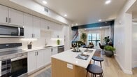 Located in Millcreek, Utah, this thoughtfully designed one-bedroom, one-bathroom residence offers a contemporary open-concept layout that maximizes every square foot. The combined kitchen, dining, and living area forms the heart of the home, anchored by a striking kitchen featuring white shaker cabinetry with matte black hardware, quartz countertops, a tile backsplash, stainless steel appliances, and a wood-accented island with bar seating. Light wood-tone flooring flows throughout, enhancing the bright, airy atmosphere created by recessed lighting. The living area makes a bold statement with a dramatic teal accent ceiling and a large window that frames outdoor views while flooding the space with natural light, opening to a private patio. The bedroom is a calm retreat, highlighted by a two-tone sage green accent wall, direct patio access through floor-to-ceiling windows, and a dedicated walk-in closet. The bathroom features warm wood vanity cabinetry, sage green wainscoting, light wood-tone flooring, and a full tub-shower combo with clean white tile. Additional conveniences include a dedicated laundry area, utility room, hallway, and closet, making this a highly functional and stylish Millcreek residence.