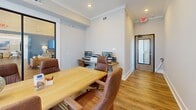 Located at 723 W 19th St in Panama City, Florida, this single-room office is a thoughtfully designed professional workspace that balances functionality with a polished aesthetic. The room is finished with warm hardwood-style flooring, crisp white walls accented by crown molding, and recessed lighting that creates a clean, well-lit environment.

At the heart of the space sits a solid wood conference table surrounded by brown leather executive chairs, making it well-suited for meetings and collaborative work. A large wall-mounted flat-screen display is positioned prominently on one wall, ideal for presentations and video conferencing. Along the rear wall, a dedicated workstation area features dual computer monitors and a printer, providing a functional zone for individual tasks.

A floor-to-ceiling window dressed with sheer, patterned drapery allows generous natural light to filter into the room while maintaining privacy. The window offers a glimpse of the exterior, lending the space an open, airy feel despite its compact footprint. A decorative globe on the conference table adds a refined touch to the overall décor.

The office is accessible via a glass-panel entry door, and its layout is efficient and purposeful, accommodating both collaborative and independent work seamlessly. This space is well-suited for small teams or professionals seeking a refined, move-in-ready office environment.
