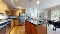 This single-floor residence offers a thoughtfully designed open-concept layout that seamlessly connects the kitchen, dining, and living areas. The kitchen is a standout feature, equipped with warm honey-toned shaker cabinetry, dark granite countertops, stainless steel appliances including a refrigerator, microwave, range, and dishwasher, and a central island with pendant lighting above. Hardwood flooring flows throughout the kitchen and transitions into the adjoining areas, adding warmth and continuity.

The living room is bright and inviting, with large windows fitted with blinds and curtains that allow generous natural light to fill the space. A ceiling fan adds comfort, and the room provides ample space for a full seating arrangement. The dining area is positioned adjacent to a sliding glass door, offering outdoor access and views of surrounding greenery.

Two well-sized bedrooms feature plush carpeting, natural light from windows with decorative curtains, and a cohesive blue and neutral color palette that gives each room a calm, restful ambiance. The bathroom is finished with warm wood-tone cabinetry, a tiled tub-shower combination, and durable wood-look flooring. Throughout the residence, the design reflects a consistent and polished aesthetic that balances comfort with modern style.