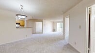 This well-appointed apartment offers 950 square feet of single-floor living space, thoughtfully laid out with four bedrooms, two full bathrooms, and a dedicated closet. The entrance opens toward a combined kitchen and living room area. The kitchen features light wood cabinetry, wood-look luxury vinyl flooring, a double sink, and black appliances including a refrigerator, electric range with overhead exhaust, and dishwasher. The adjacent living room is carpeted and benefits from a sliding glass door that opens onto a private balcony, providing outdoor views of the surrounding community and mature trees. A pendant light fixture illuminates the dining transition area, which also features wood-look flooring. The four bedrooms are carpeted and receive natural light through horizontal-blind-fitted windows. The primary bedroom measures 150 square feet. The two full bathrooms each include a tub/shower combo with white tile surround, a toilet, a wood-toned vanity, and wood-look vinyl plank flooring. A carpeted hallway connects the bedrooms and bathrooms, with panel-style doors throughout. Textured ceilings are present in the living and bedroom areas, contributing to the unit's classic apartment aesthetic.