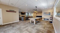This well-appointed single-floor amenity center offers a generous layout designed for both recreation and fitness. The main gathering area is an expansive, open-plan game and lounge room finished with patterned carpet tiles and a drop tile ceiling with recessed and pendant lighting. A centerpiece pool table anchors the space, complemented by a leather sectional seating area, a wall-mounted flat-screen TV, and a brick fireplace that adds warmth and character. A bar-height counter with bar stools provides an additional social gathering spot, while decorative artwork enhances the inviting atmosphere throughout.

The fitness room is thoughtfully outfitted with rubber flooring, cardio machines including treadmills and an elliptical, a full dumbbell rack, an adjustable weight bench, stability balls, and resistance equipment. Motivational wall lettering — including "Discipline," "Sweat," and "Sacrifice" — reinforces the room's energetic purpose. Natural light enters through multiple windows, and a wall-mounted TV adds convenience for workout sessions.

Two ADA-accessible bathrooms serve the facility, each featuring luxury vinyl plank flooring, grab bars, and clean, neutral finishes. One bathroom includes a vanity with a marble-style countertop and framed mirror, elevating the overall level of finish throughout this well-rounded amenity space.