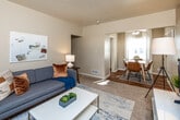 This efficiently designed one-bedroom, one-bathroom unit in Des Moines, Iowa offers a well-organized single-floor layout that maximizes its compact footprint. The living room features neutral-toned carpet, warm beige walls, and a large window dressed with navy curtains that allows natural light to fill the space. The open sightline connects the living area directly to the dining space, where hardwood flooring begins and a windowed nook provides a bright setting for a small dining table.

The kitchen is outfitted with warm oak cabinetry, a double-basin sink, stainless steel refrigerator, and hardwood floors, accompanied by a window that brings in additional natural light. A hallway connects the main living areas to the private bedroom, which features plush carpeting, a window with curtain panels, and soft, neutral walls that create a calm atmosphere suited for rest.

The bathroom includes a full-size soaking tub with a shower combination, white tile surround, and a windowed wall that provides ventilation and light. Throughout the unit, a consistent warm neutral color palette and natural light from multiple windows contribute to a cohesive and livable ambiance suited for single occupancy in Des Moines.