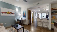 This single-floor unit showcases a contemporary design with polished concrete floors running throughout the main living areas, creating a sleek, urban aesthetic. The open-concept layout connects the living area, dining space, and kitchen, promoting a seamless flow between rooms.

The living area features a muted blue accent wall, ceiling fan, and wall-mounted lighting, lending a relaxed yet modern atmosphere. A built-in desk nook provides a functional workspace within the living space. Large windows and a glass sliding door bring in abundant natural light, while the balcony—accessible from both the living area and bedroom—offers open views of the surrounding cityscape.

The kitchen is well-appointed with light maple cabinetry, dark countertops, and a full suite of stainless steel appliances, including a refrigerator, range, and over-the-range microwave. A breakfast bar with seating provides additional dining options.

The bedroom is comfortably scaled with carpeted flooring, a sliding glass door to the private balcony, and a closet with sheer curtain panels. The full bathroom features maple vanity cabinetry, dark countertops, a tub-shower combination, and tile flooring, offering a clean and functional design.
