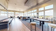 Located at 8331 S Valley Hwy in Englewood, Colorado, this contemporary amenity space offers a generously sized, single-floor layout designed for social gathering and relaxation. The open-plan interior is defined by soaring ceilings, floor-to-ceiling windows, and expansive clerestory glazing that flood the space with abundant natural light and frame sweeping views of the surrounding Englewood skyline and outdoor terrace.

The main lounge area features elegant hardwood-style flooring, plush sectional seating arranged over layered area rugs, and a full-size billiards table illuminated by sleek pendant lighting. Circular statement light fixtures add a refined architectural touch throughout. A dedicated dining and casual seating zone accommodates multiple table configurations — from intimate two-tops to communal high-top bar tables — ideal for both individual use and group gatherings.

The fully equipped kitchen area is outfitted with modern gray cabinetry, white quartz countertops, a striking slatted wood accent wall, stainless steel appliances, and elegant pendant lighting. A secondary prep counter features a dark stone surface, adding a refined contrast to the overall design palette.

Double glass doors lead directly to an outdoor terrace, complete with additional seating, extending the social experience into the open air with panoramic views of the Colorado landscape.