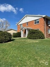 Inviting brick apartment building with manicured lawn and bright windows under a clear blue sky. - Allison West Apartments