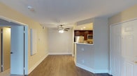 This single-floor unit offers a practical and inviting layout designed to maximize its comfortable footprint. The open-concept living area features warm hardwood-style flooring that flows throughout the space, complemented by soft yellow-toned walls and crisp white baseboards that lend a bright, clean aesthetic. A ceiling fan with a light fixture is centrally positioned overhead, providing both air circulation and ambient lighting to the main living area.

The kitchen is accessible via a peninsula-style breakfast bar that separates it from the living space while maintaining an open feel. Dark espresso cabinetry contrasts with the light countertops, and stainless steel appliances — including a refrigerator and microwave — give the kitchen a modern, polished look. Recessed lighting illuminates the kitchen area effectively. Ceiling-height transitions and a neatly framed pass-through opening add architectural interest. The overall ambiance is clean, functional, and move-in ready, making this a well-designed one-bedroom residence suited for everyday living.