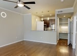 Unit #1103 at Bell Starwood in Frisco, Texas is a thoughtfully designed 1-bedroom, 1-bathroom apartment spanning 590 square feet across a single floor. The open-concept living room serves as the heart of the unit, featuring rich hardwood-style flooring, crown molding, a ceiling fan, and a classic tiled fireplace with a white mantel. Multiple windows fitted with plantation shutters allow natural light to fill the space. The kitchen is equipped with granite countertops, dark espresso cabinetry, a stainless steel refrigerator, and a breakfast bar with pendant lighting overhead — ideal for casual dining and entertaining. A dedicated nook with granite countertop and under-cabinet lighting provides a functional workspace or built-in desk area. The 150-square-foot primary bedroom offers plush carpeting, crown molding, a ceiling fan, and a window with outdoor views. It provides direct access to both a walk-in closet and the full bathroom. The bathroom features a dark-toned vanity with granite countertop, a framed mirror, hardwood-style flooring, and a shower-tub combination. A dedicated laundry area adds everyday convenience to this well-appointed apartment.