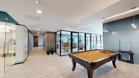 Located at 169 North Main Street in Port Chester, NY, this thoughtfully designed amenity floor spans a generous footprint and offers an impressive array of wellness, fitness, and social spaces. The layout is anchored by a fully equipped gym featuring multi-station cable machines, free weights, and a dedicated yoga and stretching studio enclosed in full-height glass walls with hardwood flooring. Three sauna rooms provide a premium wellness experience, finished in warm cedar wood with glass enclosures, complemented by a tiled steam room and two well-appointed bathrooms nearby. Two modern kitchens serve the space, each outfitted with wood-grain cabinetry, light quartz countertops, subway tile backsplashes, and stainless steel appliances — ideal for entertaining or everyday use. The lounge areas exude a sophisticated ambiance, with slate-blue paneled accent walls, curated artwork, and stylish furnishings including leather sofas and chaise chairs. Large folding glass doors open to an outdoor courtyard, flooding the interior with natural light. A billiards table anchors the social zone, while wide hallways with wood-slat accents and light tile flooring connect each area seamlessly, creating a cohesive, resort-caliber experience throughout.