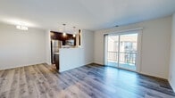 This 2-bedroom, 1-bathroom single-floor residence offers a thoughtfully designed layout that maximizes both functionality and comfort. The open-concept living room and kitchen area serves as the heart of the home, featuring light-toned hardwood-style flooring that flows throughout the main living spaces. A sliding glass door opens to a private balcony, filling the living room with natural light and providing pleasant outdoor views.

The kitchen is equipped with dark espresso cabinetry, stainless steel appliances, light countertops with a subway tile backsplash, and pendant lighting above the peninsula — creating a clean, modern aesthetic. A half-wall separates the kitchen from the living area while maintaining an open feel.

Both bedrooms are carpeted and include ceiling fans with overhead lighting. The primary bedroom is a generously sized retreat with a window that allows for natural light. The second bedroom offers a comparable level of comfort and flexibility.

The full bathroom features wood-look tile flooring, dark vanity cabinetry, and a tub-shower combination with marble-style tile surround. Additional storage is provided by a dedicated closet, and a hallway connects all areas of the home seamlessly. The overall aesthetic is clean, contemporary, and move-in ready.