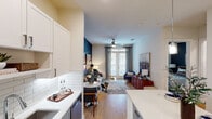 This single-floor residence offers a thoughtfully designed open-concept layout where the kitchen, dining, and living areas flow seamlessly together. The kitchen is a standout feature, showcasing tall white upper cabinetry, two-tone grey lower cabinets, white quartz countertops, and a classic subway tile backsplash. A generously sized island with a built-in wine rack and bar seating serves as both a functional workspace and casual dining hub, illuminated by sleek pendant lighting. Stainless steel appliances, including a French door refrigerator, complete the space. Light wood-tone flooring extends throughout the main living areas, enhancing the sense of continuity and warmth.

The living room makes a strong visual statement with a deep navy accent wall, a ceiling fan, and large windows dressed with patterned drapes that invite natural light. The bedroom echoes this design with its own bold dark accent wall, ceiling fan, and multiple windows providing ample daylight.

The bathroom features white subway tile surrounding the tub-shower combination and dark tile flooring. A doorway from the bathroom leads directly into a walk-in closet equipped with tiered shelving, hanging rods, and an in-unit washer and dryer — a practical and convenient configuration throughout.