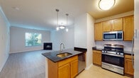 This single-floor residence offers a thoughtfully designed open-concept layout that seamlessly connects the kitchen, dining, and living areas. The kitchen is a functional centerpiece, featuring warm honey-toned cabinetry, dark granite countertops, a classic white subway tile backsplash, and a full suite of stainless steel appliances including a gas range, built-in microwave, refrigerator, and dishwasher. A kitchen island with an integrated sink and pendant lighting above adds both style and practicality.

The living area is bright and welcoming, anchored by a fireplace with a sleek dark surround and framed by large windows that invite abundant natural light and views of surrounding greenery. Crown molding accents the ceiling, adding an elegant finishing touch throughout the main living space. Light hardwood-style flooring runs through the main areas, while plush carpet provides comfort in the bedroom, which features a bright window with blinds for privacy.

The bathroom is clean and functional, offering a full tub-shower combination with white tile surround, a curved shower rod, and a vanity with warm wood cabinetry. The entryway provides a smooth transition into the home with easy access to the kitchen and main living spaces, completing a cohesive and practical floor plan.