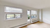 This well-appointed unit at 2386 New St in Burlington, Ontario presents a clean, modern aesthetic throughout its single-floor layout. The galley-style kitchen is thoughtfully designed with white flat-panel cabinetry extending to the ceiling, light quartz countertops, a stainless steel undermount sink, and a full suite of stainless steel appliances including a refrigerator, stove, and built-in microwave. Large-format tile flooring grounds the space with a crisp, contemporary feel.

The living area is a standout feature, bathed in natural light from multiple windows and a glass door that opens directly onto a private balcony. The elevated position of the unit affords open views of the Burlington skyline and surrounding greenery. Light hardwood-style flooring flows throughout the living spaces and bedrooms, enhancing the bright, airy atmosphere. Baseboard heating is present throughout.

The bedrooms are generously proportioned, with large windows framing outdoor views and well-organized closets featuring wire shelving systems. The bathroom is finished with neutral tile, a full soaker tub with a tiled surround accented by mosaic detailing, a white vanity with an undermount sink, and chrome fixtures.
