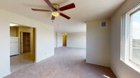 This single-floor residence offers a thoughtfully laid-out living space with a clean, neutral aesthetic throughout. The expansive main living area is covered in plush wall-to-wall carpeting and is anchored by a ceiling fan with wooden blades, providing both comfort and airflow. A textured ceiling adds character to the room, while a sliding glass door and large windows bathe the space in natural light and offer sweeping views of lush greenery and the surrounding landscape.

The kitchen is equipped with dark, glossy cabinetry that contrasts with light countertops, and includes a gas range, dishwasher, and a double sink — providing ample functionality for everyday cooking. The light tile flooring in the kitchen complements the overall neutral palette of the residence.

The bedrooms are generously sized, each featuring soft carpeting, large windows with scenic views, and closet space. The layout provides a comfortable sense of openness and privacy throughout.

The bathroom features a wide vanity with an integrated sink, dark wood cabinetry below, a large mirror, white tile wainscoting, and decorative mosaic tile flooring, creating a clean and functional space.

Overall, the residence presents a bright, open atmosphere with practical finishes and pleasing outdoor views.