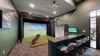 This single-floor indoor golf simulator facility is thoughtfully designed to deliver an immersive golfing experience year-round. The space is anchored by a professional-grade hitting bay equipped with a Foresight Sports launch monitor and a high-definition projector that casts lifelike course visuals onto a large impact screen. A synthetic turf hitting mat provides a realistic surface for full swings, and protective netting flanks the bay to ensure safety during play.

The interior is finished with deep forest green walls that lend a sophisticated, golf-club-inspired ambiance throughout. Patterned carpet with a subtle golf-course motif covers the floors, tying the theme cohesively together. A built-in bar-height counter with comfortable upholstered bar stools runs along one side of the simulator room, offering spectators an ideal vantage point. A secondary monitor mounted behind the counter allows viewers to track shot data and gameplay in real time. Open storage cubbies nearby provide convenient space for equipment and personal items.

Adjacent to the simulator bay is a dedicated reception area, complete with a front desk, a low credenza with cabinetry, and golf-themed black-and-white photography displayed on the walls. Recessed lighting throughout keeps the space well-lit, while a glass-paneled entry door connects the facility to the broader building. The overall design balances functionality with a refined, club-house aesthetic.